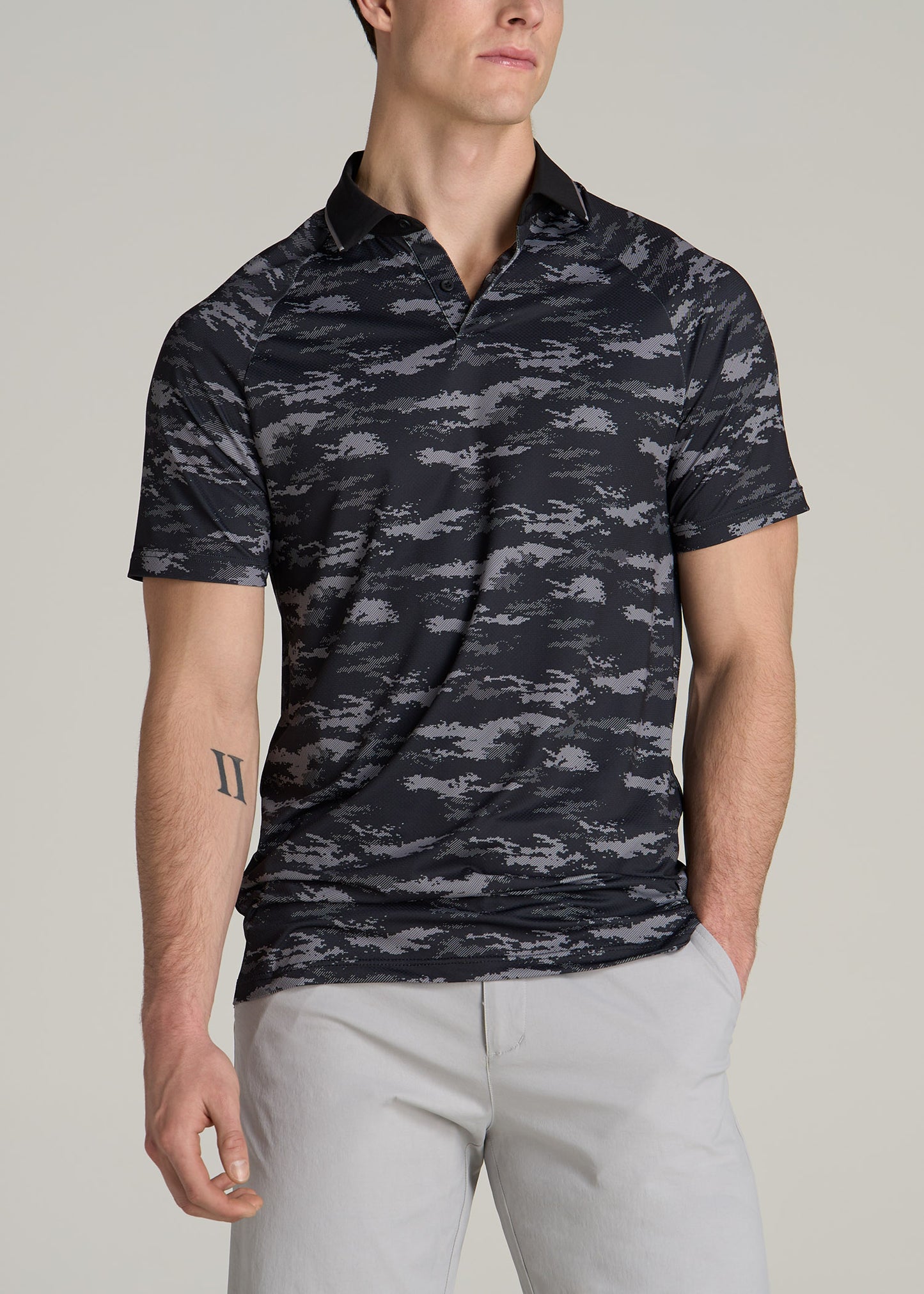A tall man wearing American Tall's Contrast Collar A.T. Performance Print Golf Tall Men's Polo Shirt in Black and Grey Camo.