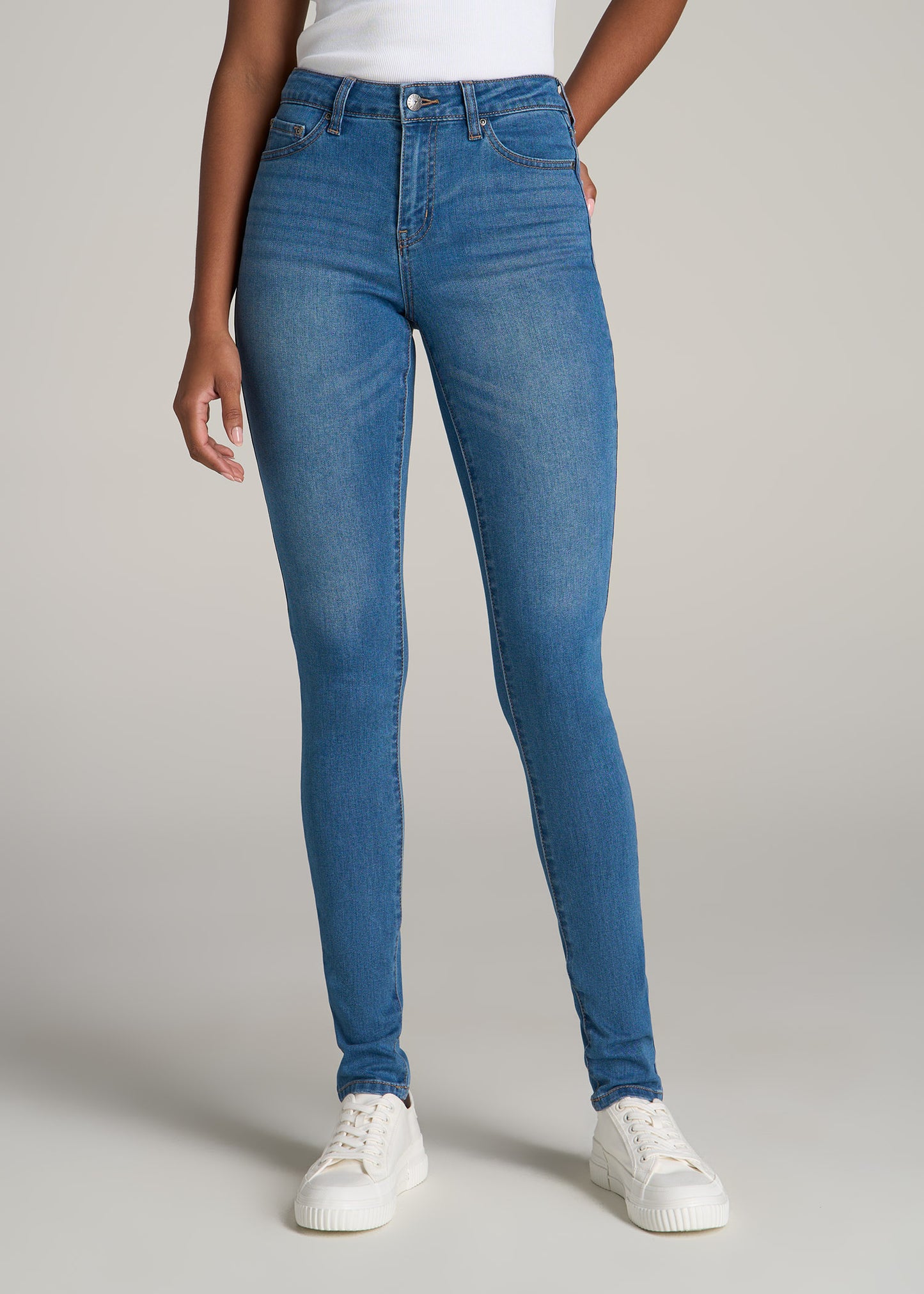 A tall woman wearing American Tall's Sarah Mid-Rise Skinny Jean in Bright Mid Blue.