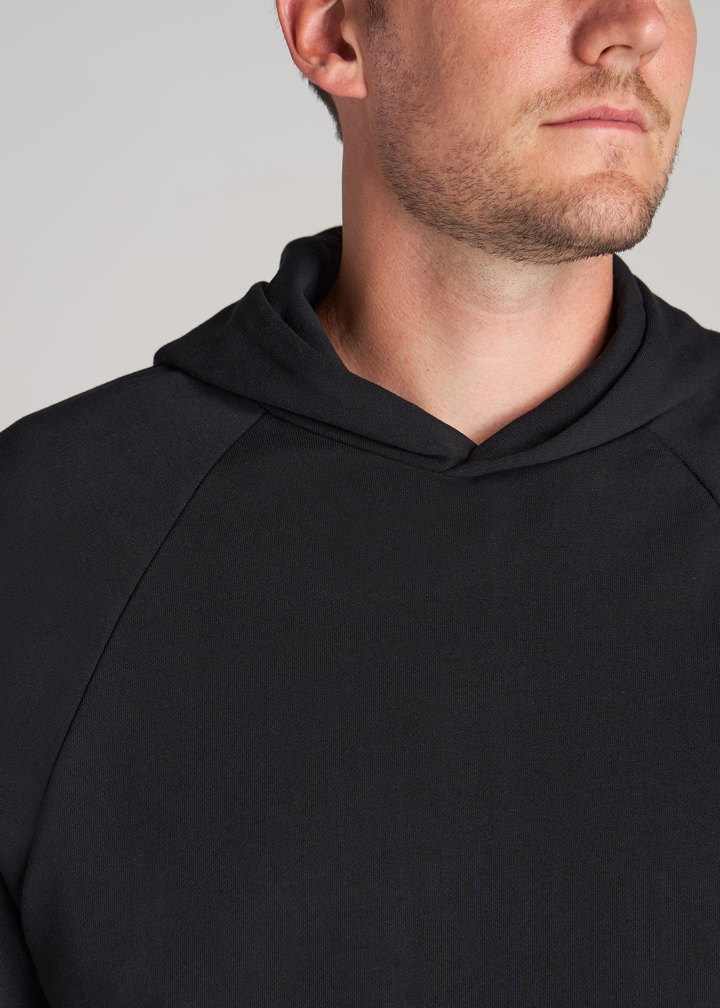 A tall man wearing American Tall's Wearever French Terry Raglan Men's Tall Hoodie in Black.