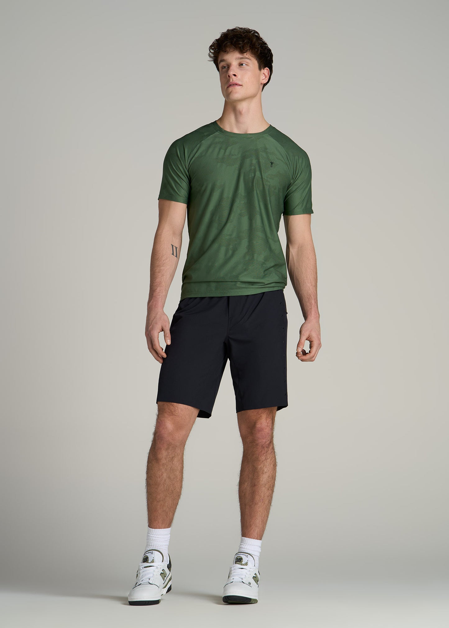 A tall man wearing American Tall's Featherweight Perforated Training Shorts in Black and Raglan Training T-Shirt in Forest Green.
