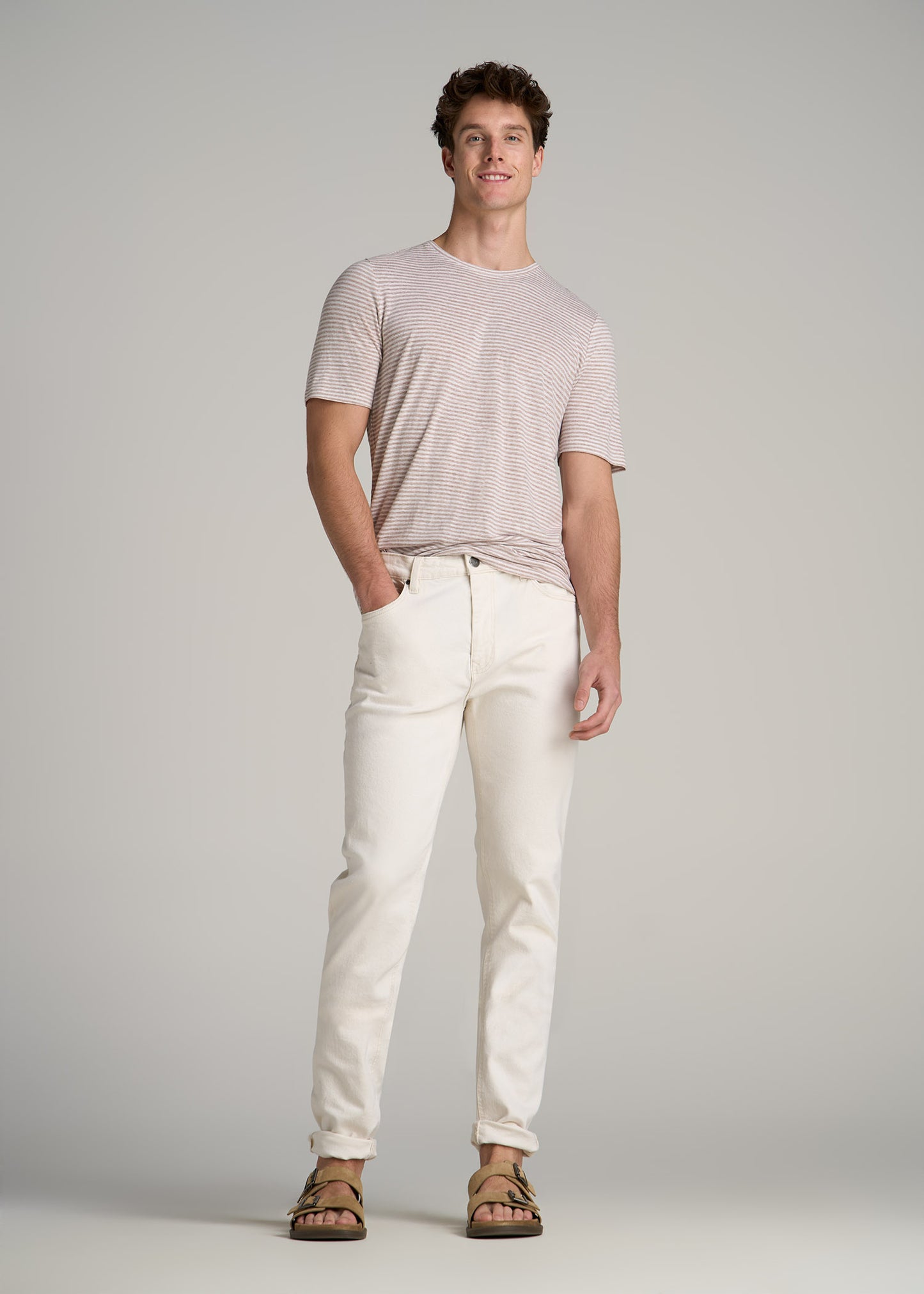 A tall man wearing American Tall's Linen Crewneck T-Shirt in Beige and White Stripe
and Milo Relaxed Tapered Jeans in Ecru Buff.