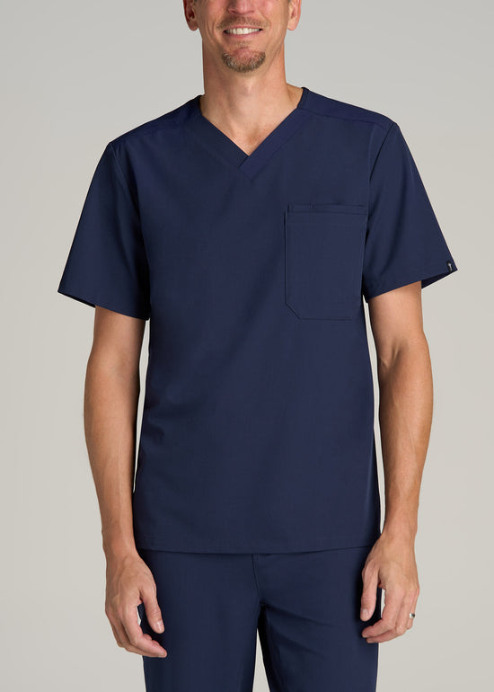 A tall man wearing American Tall's Short-Sleeve V-Neck Scrub Top in the color Patriot Blue.