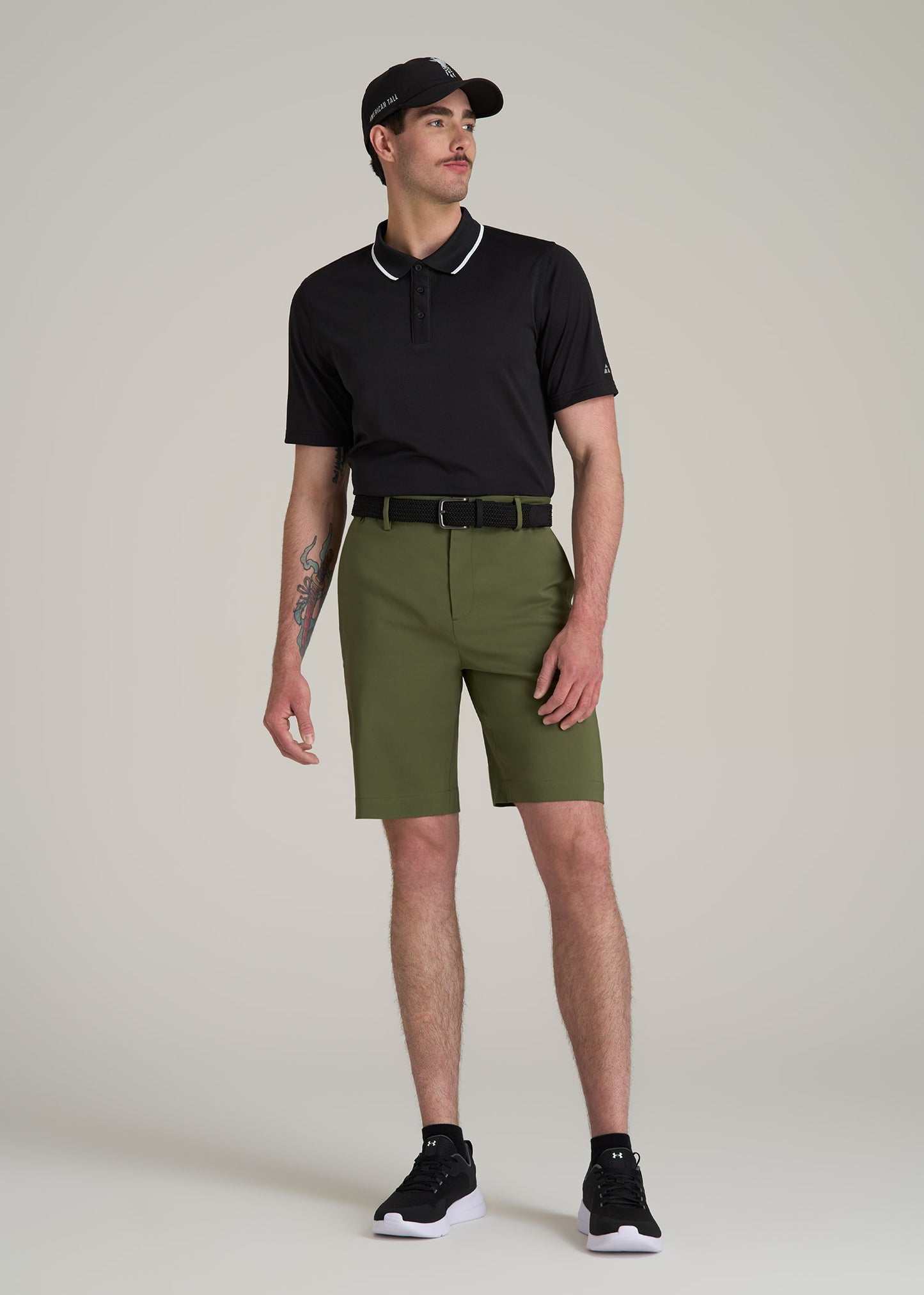 A tall man wearing American Tall's Tech Chino Shorts in Bright Olive, Performance Tipped Golf Polo in Black and a Stretch Woven Belt in Black.