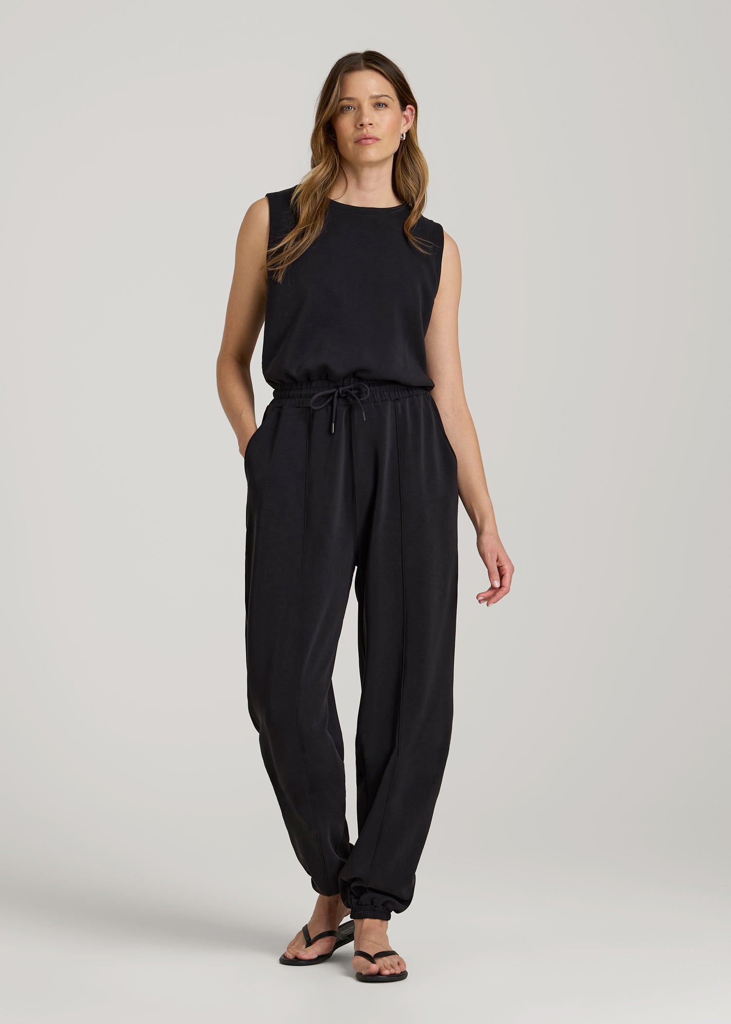 Tall woman wearing the American Tall Soft Motion Sleeveless Sweatpant Jumpsuit in Black, styled for lounging and travel days