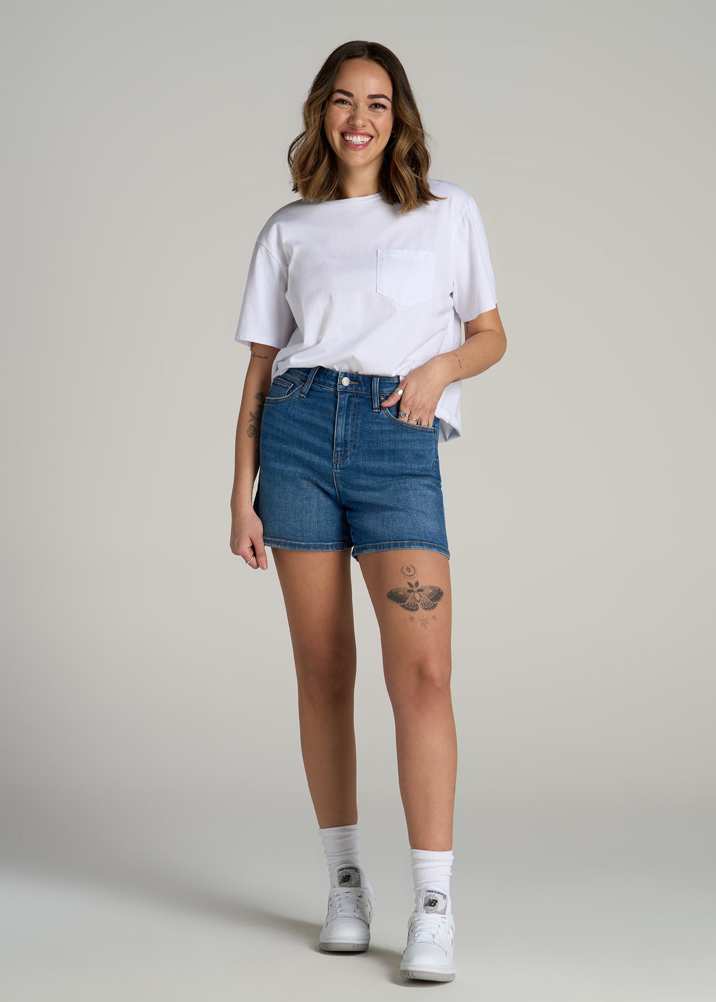 A tall woman wearing American Tall's High Rise Denim Shorts for Tall Women in Classic Mid Blue.