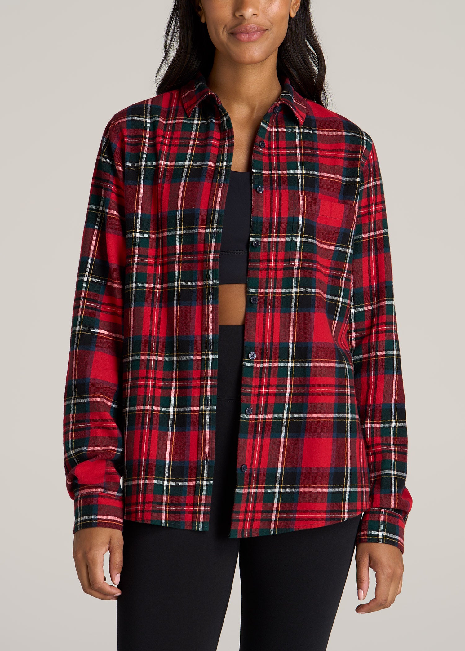 A tall woman wearing American Tall's Flannel Button-Up Shirt in red and green tartan with black leggings.