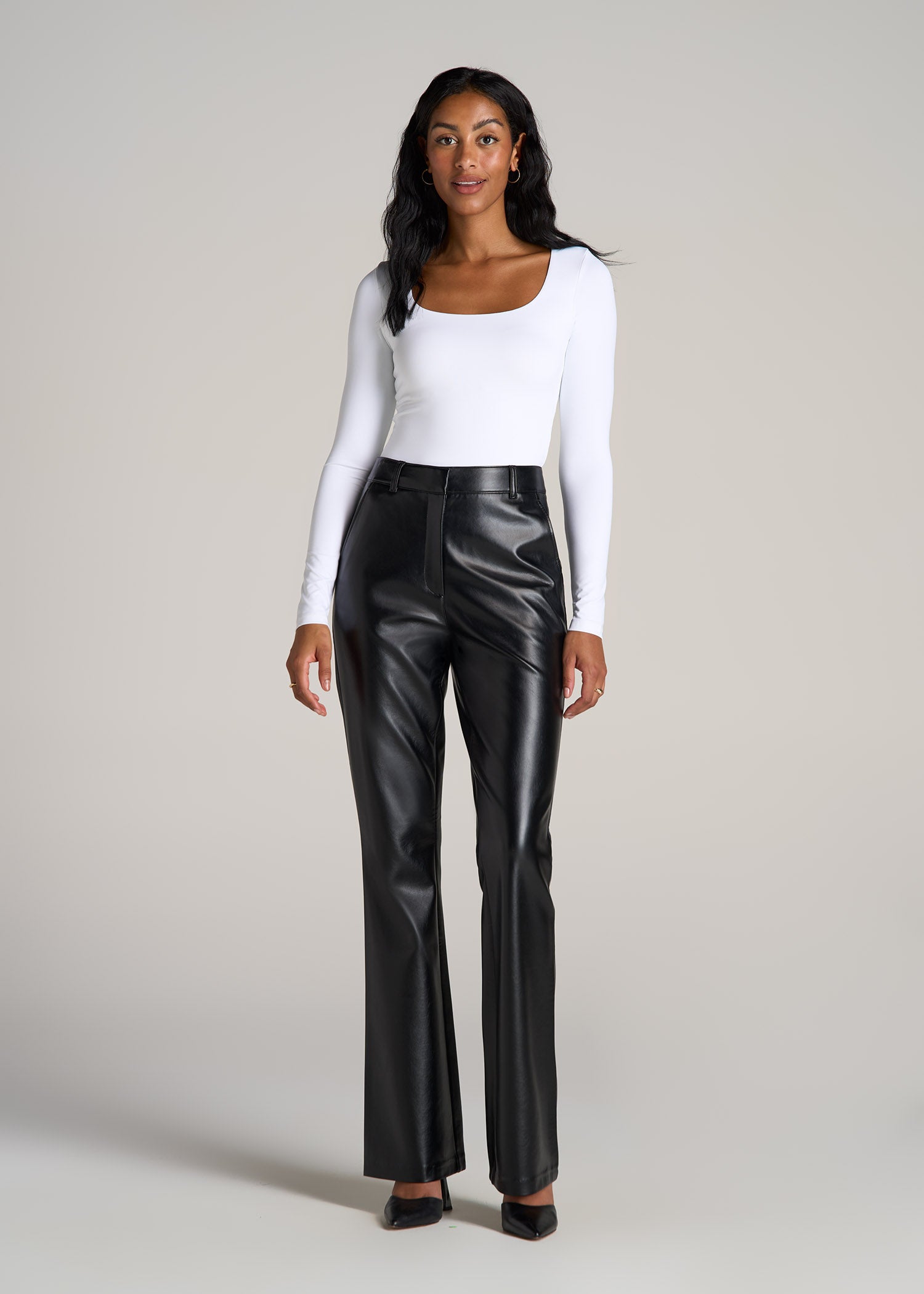 A tall woman wearing American Tall's High-Rise Flare Faux Leather Pants in the color Black.