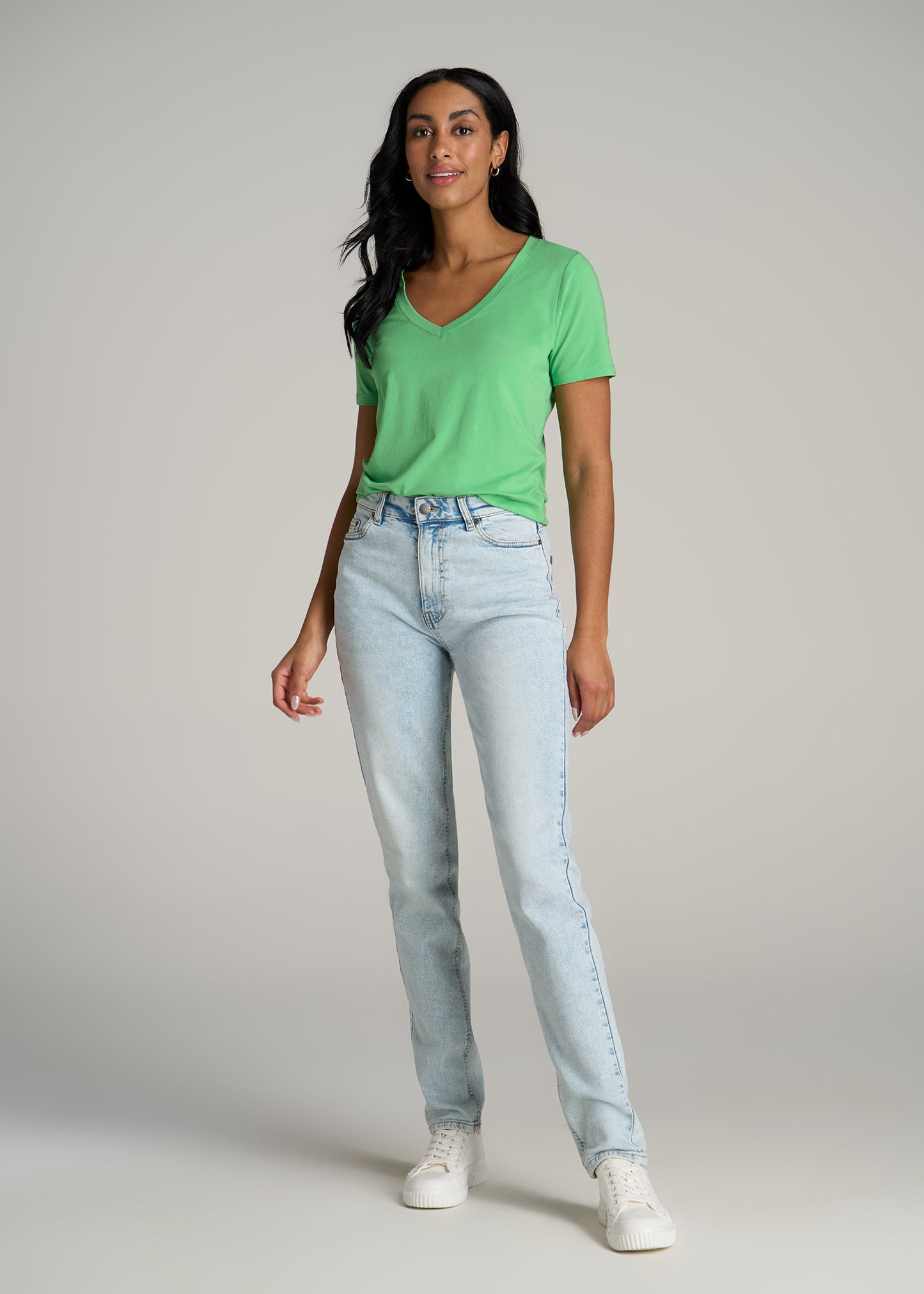 A tall woman wearing American Tall's Scoop V-Neck Tee in Matcha and Emma High Rise Relaxed Jeans in Vintage Light Indigo.
