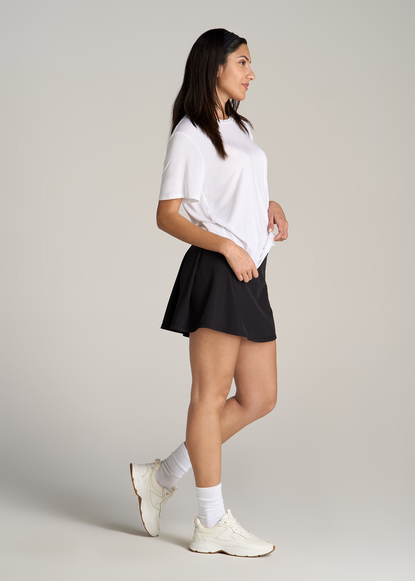 A tall woman wearing American Tall's Crewneck Pocket Tee in White and Athletic Skort in Black.