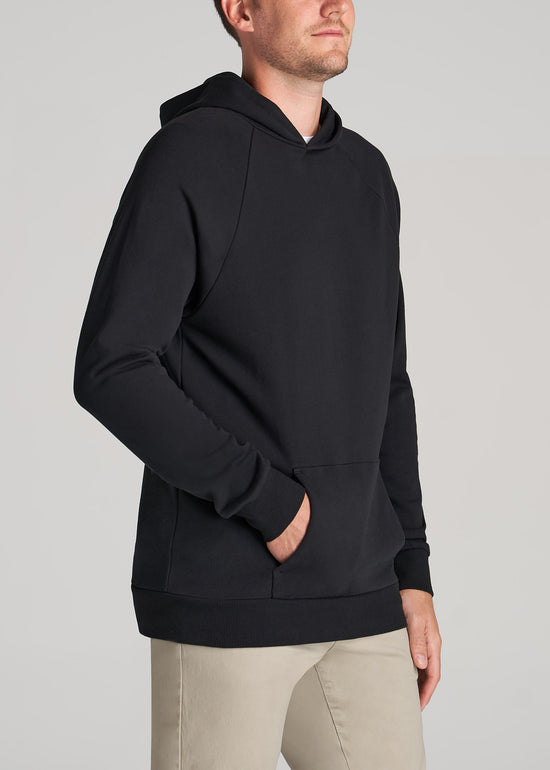 A tall slim man wearing American Tall's Wearever French Terry Raglan Hoodie in the color black.