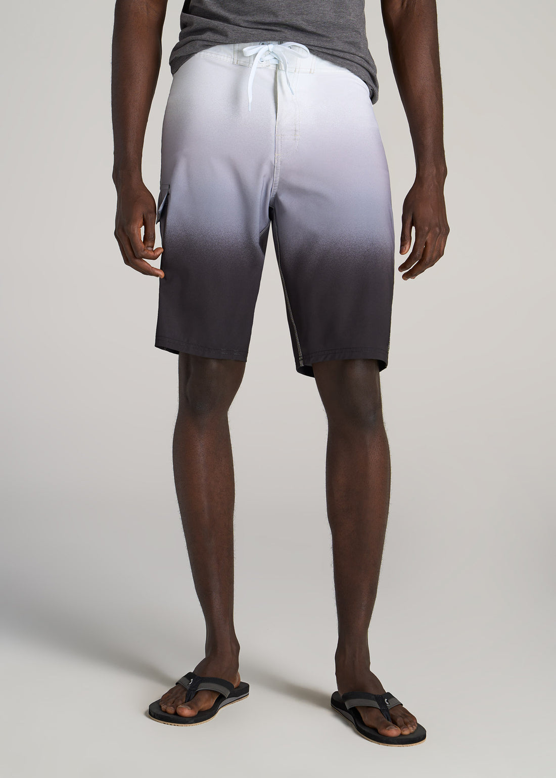 Tall man wearing white, grey and black ombre-colored board shorts.