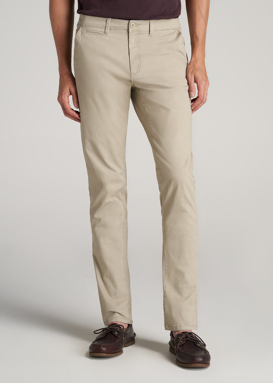 A tall man wearing cream colored tapered chinos.