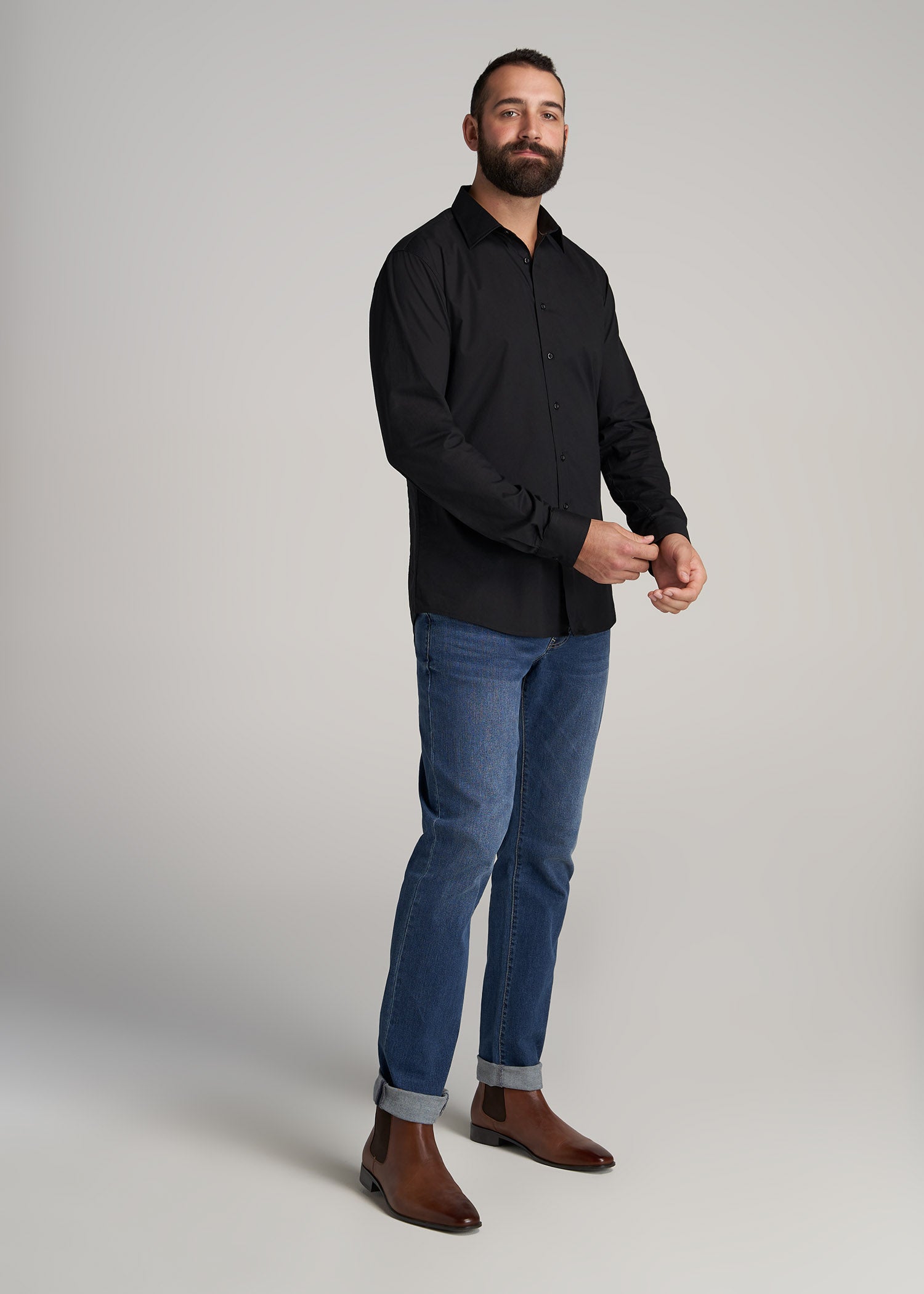 A tall man wearing American Tall's Oskar Button-Up Shirt for Tall Men in Black and Tapered Jeans for Tall Men in Blue-Steel.