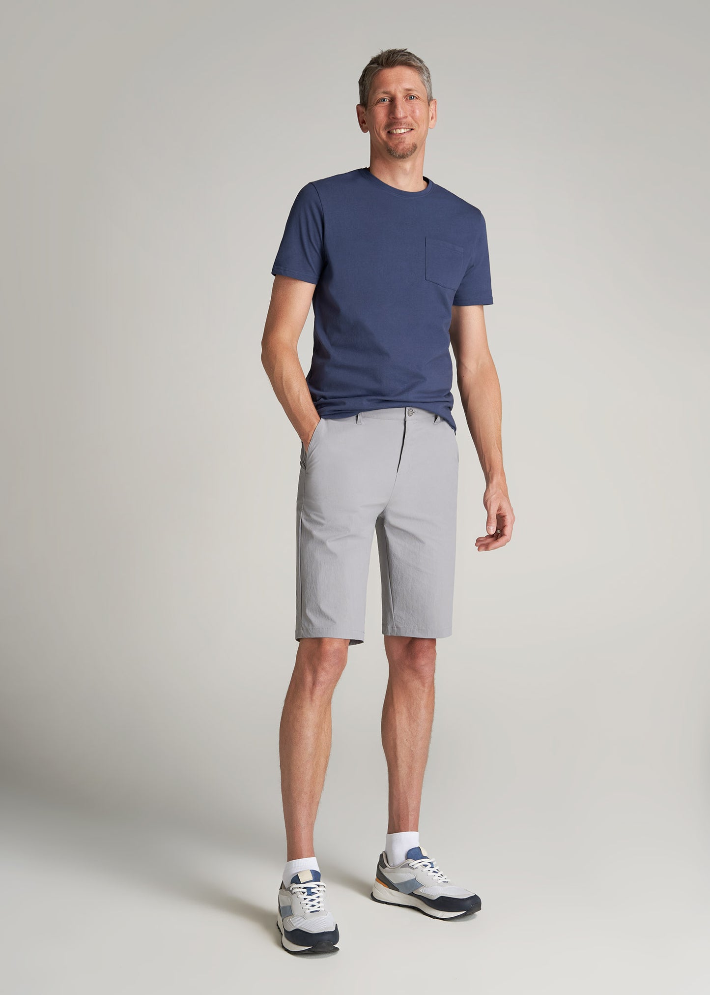 A tall man wearing American Tall's Premium Hybrid Shorts in Night Owl Grey and Everyday Pocket T-Shirt in Navy.