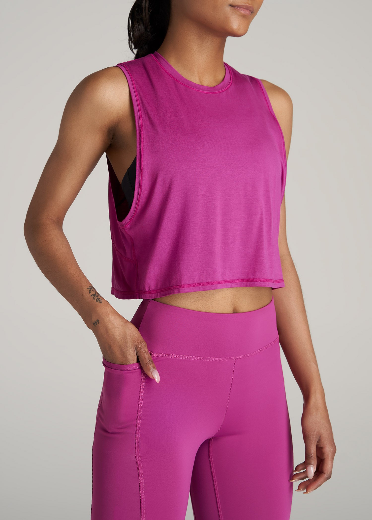 A tall woman wearing American Tall's Cropped Muscle Tank top in the color Pink Orchid and matching leggings.