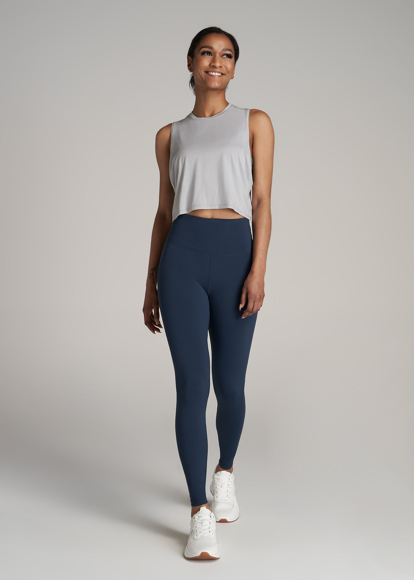 A tall woman wearing American Tall's Cropped Muscle Tank top in the color Silver.