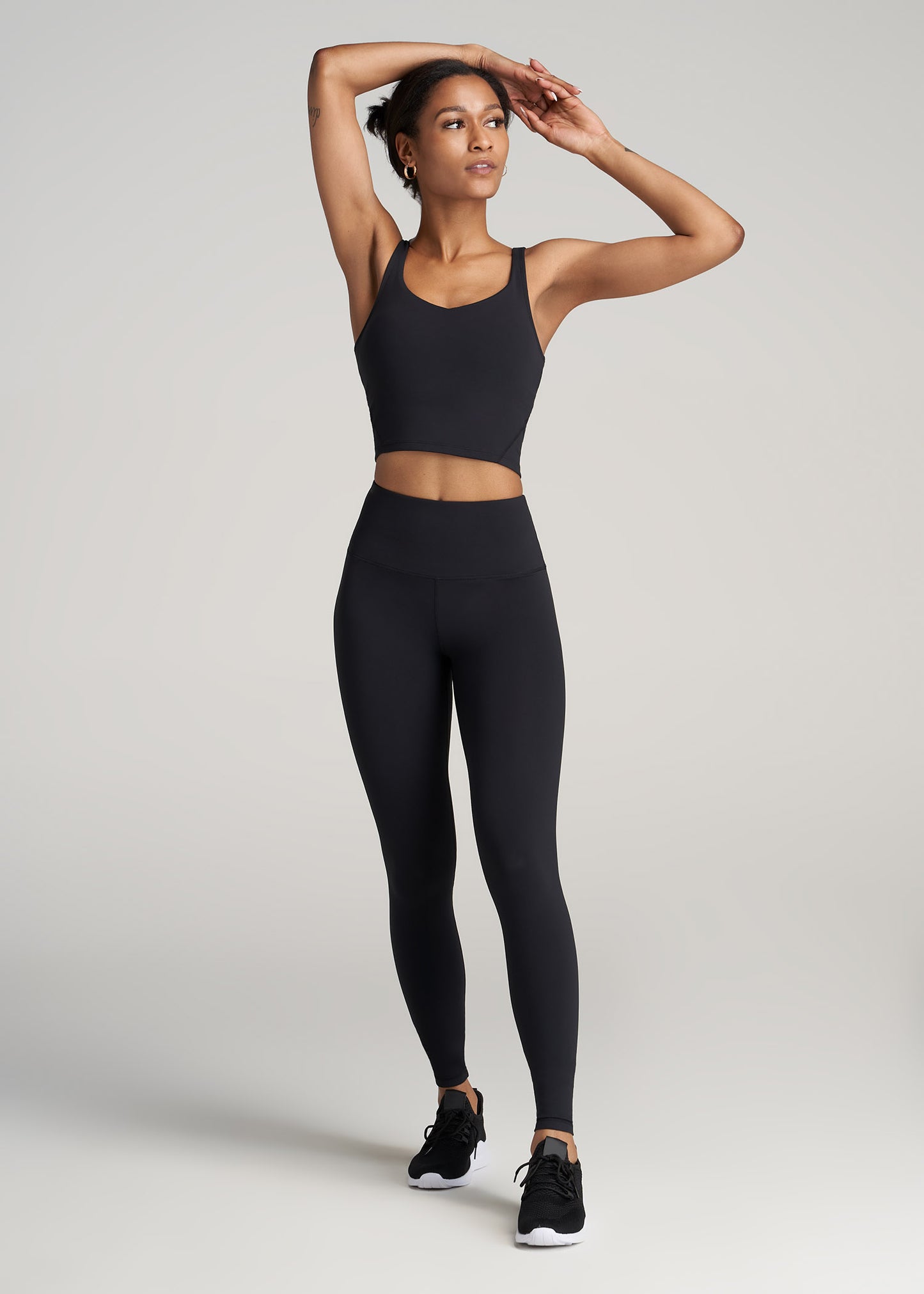 A tall woman wearing American Tall's Balance Tank Top in black with black matching leggings.