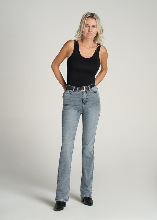 A tall woman wearing American Tall's Women's Britney Tall Bootcut Jeans in Light Grey Wash with a High Crewneck Sleeveless Bodysuit for Tall Women in Black.