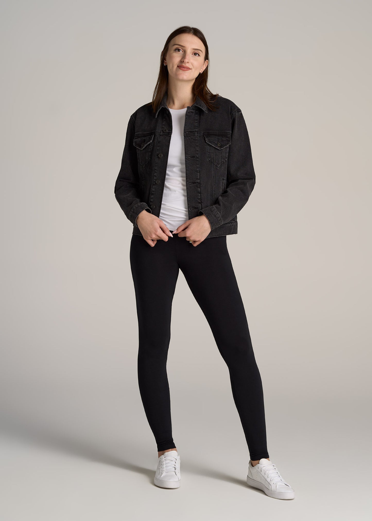 A tall woman wearing a black jean jacket and black cotton leggings.