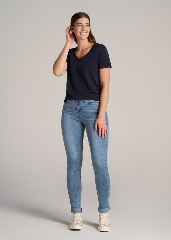 A tall woman wearing American Tall's Georgia High Rise Skinny Tall Women's Jean in Monaco Faded with their Women's Tall Scoop V-Neck Tee in Dark Navy.