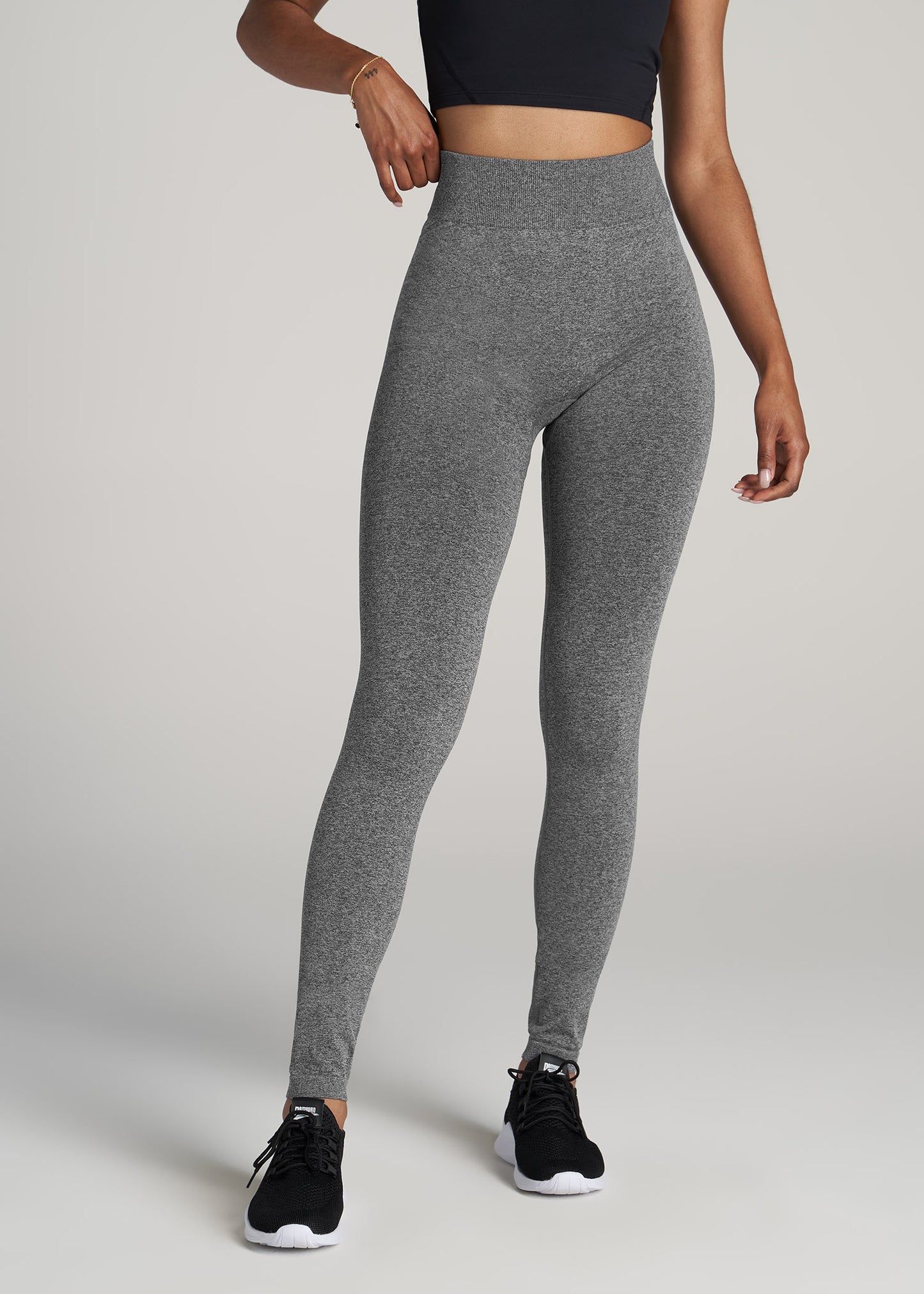 A tall woman wearing American Tall's Seamless Compression Legging in black and grey heather.