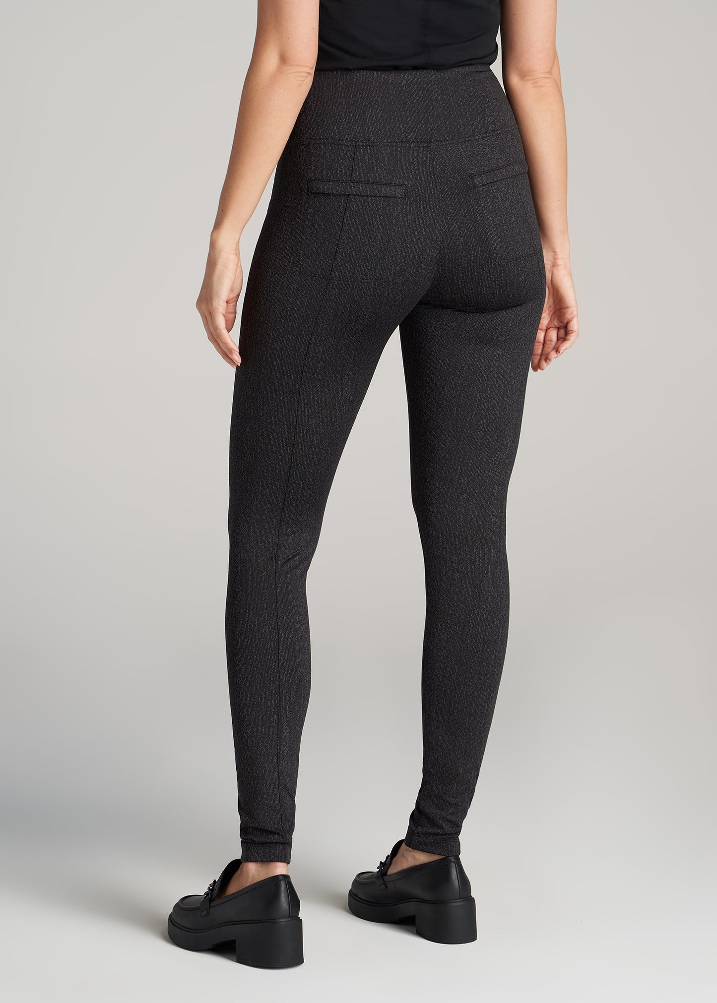 A tall woman wearing American Tall's Textured Back Pocket Legging in black charcoal.